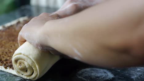 hoja plana de masa recién hecha con relleno de canela y chocolate enrollada y moldeada a mano sobre la mesa de la cocina, filmada de cerca