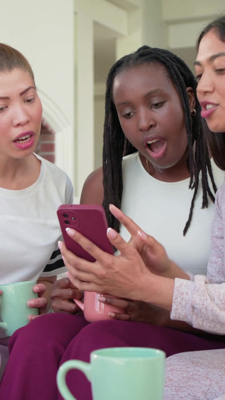 Vertical video: Flipping phone, woman with magenta phone, friends leaning on sofa at home, reacting