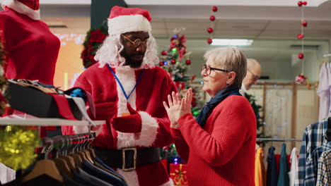 Einzelhandelsassistentin-Im-Weihnachtsmannkostüm-Hilft-Einem-älteren-Kunden-Im-Einkaufszentrum-Dabei,-Die-Rote-Bluse-Zu-Finden,-Die-Für-Die-Weihnachtspartykleidung-Benötigt-Wird.-Arbeiter-Unterstützt-ältere-Frau-Während-Der-Weihnachtszeit-Im-Modegeschäft