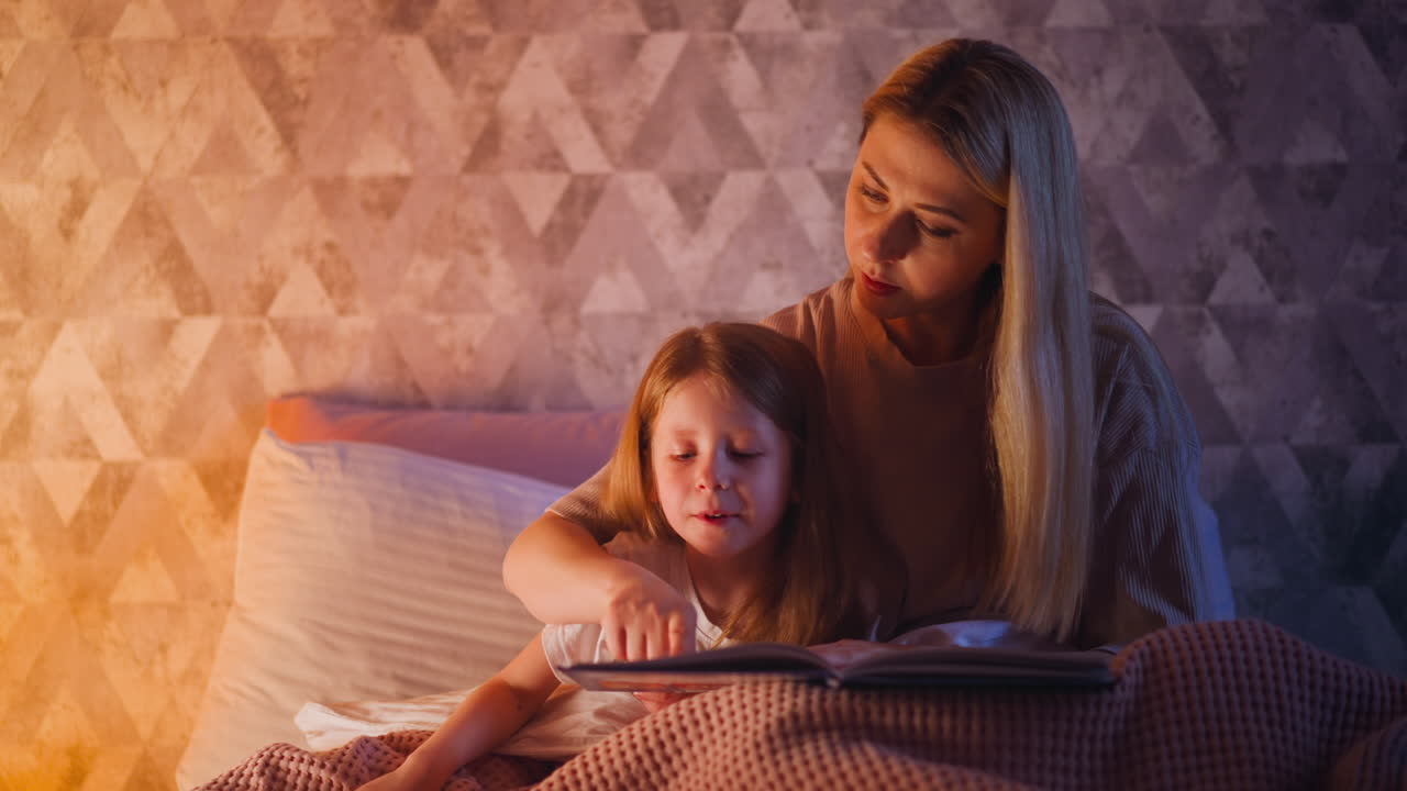 Mommy teaches girl to read following line with finger on bed