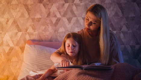 mommy teaches girl to read following line with finger on bed