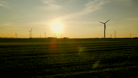 Aerial-shot---side-panning-motion-over-Puck-wind-farm-on-sunset,-rotating-wind-turbines-silhouette-sun-going-down-on-background,-Pomorskie,-Poland
