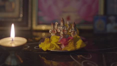 small hinduism deities statue with flowers as offerings, lit candle in foreground