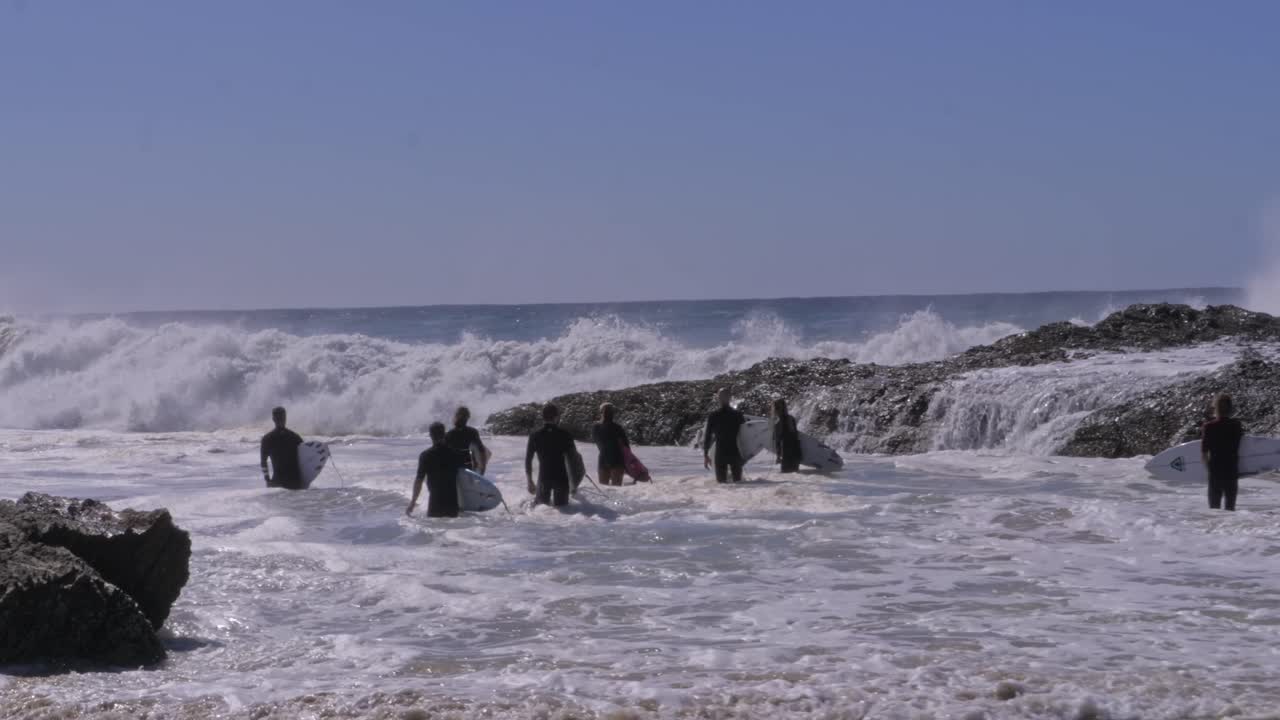 Waves Crashing On Rugged Shore With Surfers Standing At Snapper Rocks In Queensland, Australia. panning shot