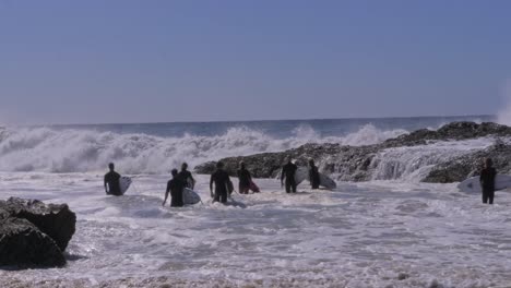 waves crashing on rugged shore with surfers standing at snapper rocks in queensland, australia. panning shot