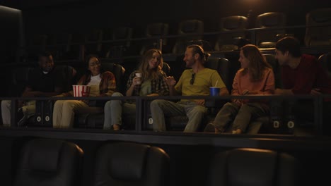 group of young friends in a movie theater, came watching a movie on a big screen, talking to each other