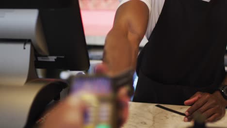 african american male barista wearing face holding payment terminal