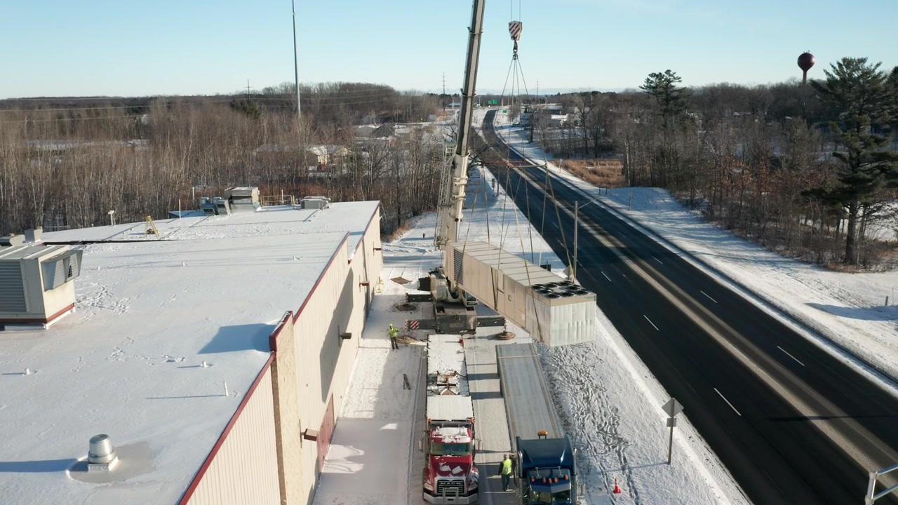 Crane lifting a new HVAC unit to be installed onto industrial building roof, aerial