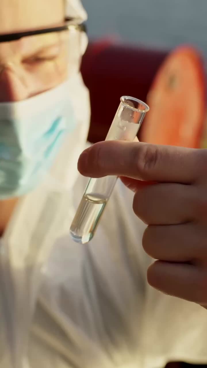 Environmental worker in white suit handling sample test tube container during water safety inspection, vertical