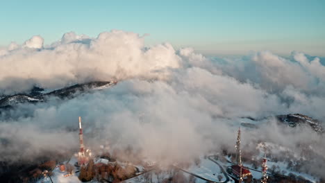 snowy mountain with communication towers above clouds at sunrise