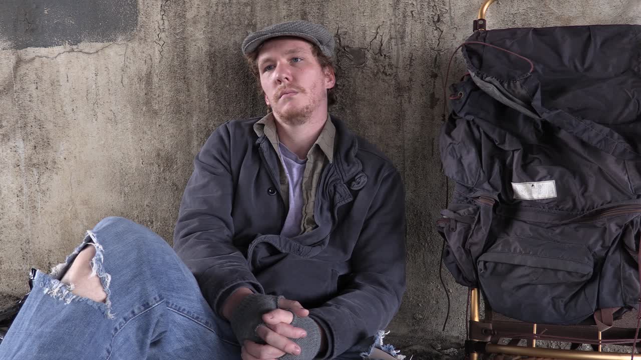 plano medio estacionario de un varón adulto joven sin hogar con desesperación en los ojos