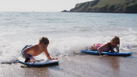 two children playing in sea with bodyboards on  summer beach vacation