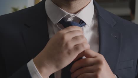 primer plano de un hombre en casa con traje de negocios alisando la corbata listo para una entrevista de trabajo