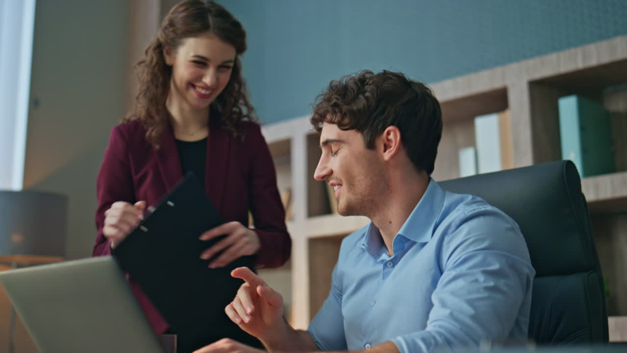 Girl manager giving report papers to smiling ceo typing laptop at office closeup