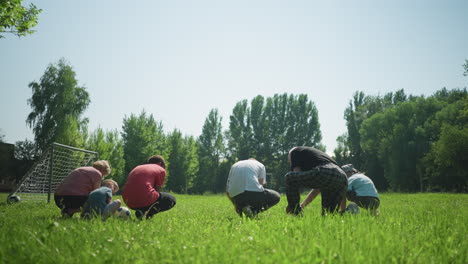 back view of a family tying their shoelaces on a sunny day, with a small goalpost nearby and a blurred larger goalpost in the background