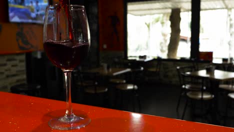 el vaso de vino vacío enfriado está lleno de líquido rojo mientras la tv juega en un fondo borroso