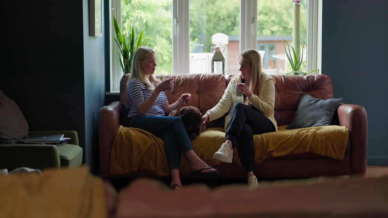 Two women having a conversation on a couch with a dog