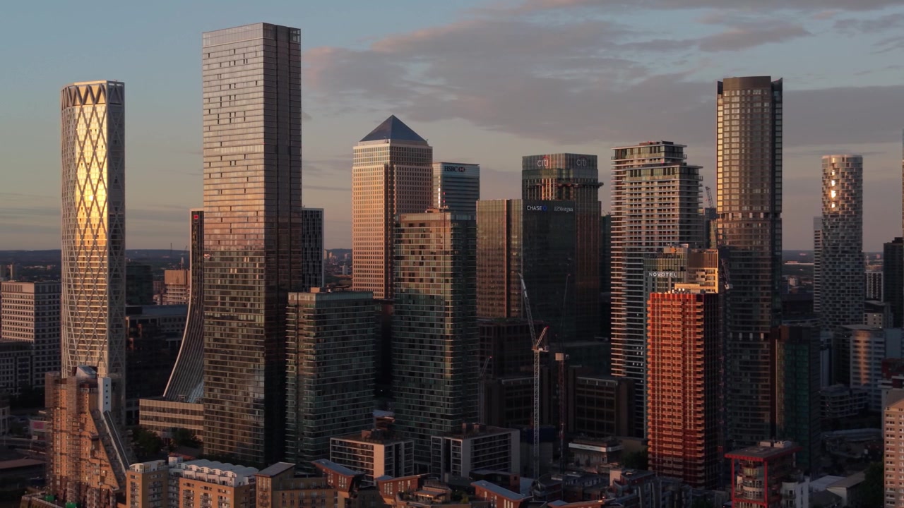 Vista del distretto finanziario di Canary Wharf, Londra, durante l'ora d'oro. La luce del sole si riflette su numerosi grattacieli moderni ed edifici per uffici. Lo skyline mostra alte strutture sotto un caldo cielo serale