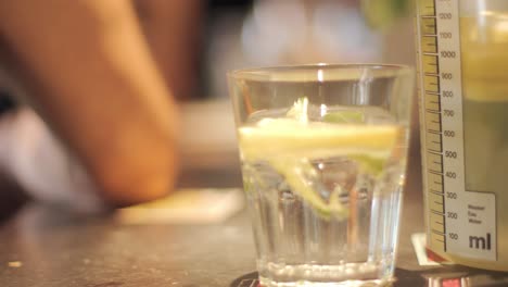 primer plano de un vaso de limonada con una rodaja de limón y una persona sentada en el fondo borroso