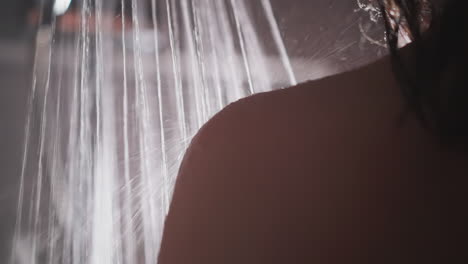 water splashes on woman shoulder in bathroom closeup. lady takes hot shower standing under strong liquid flow in washroom. regular hygienic procedure