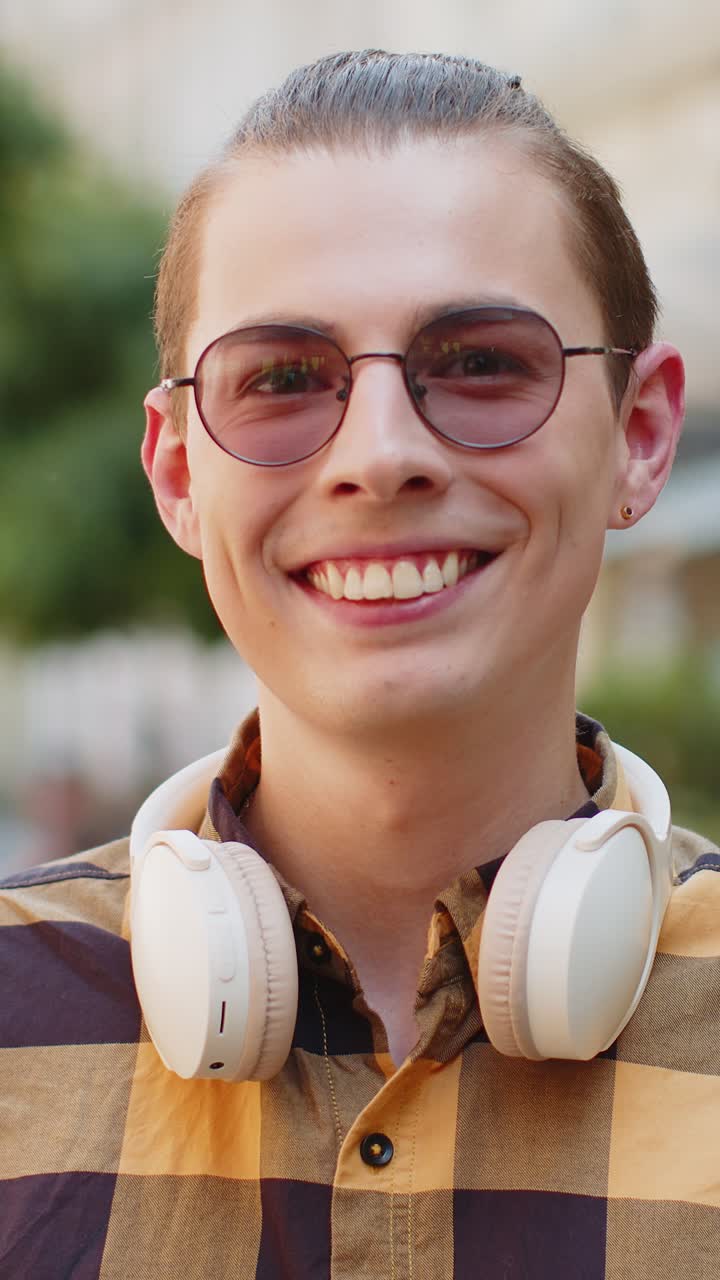 Happy smiling man listening music taking off wireless headphones looking at camera on city street