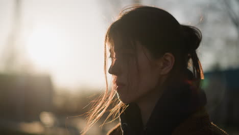 a girl walking with a heavy heart, her hair partially covering her face. the soft glow of the sunset in the background adds a somber and reflective mood, moment of introspection and melancholy