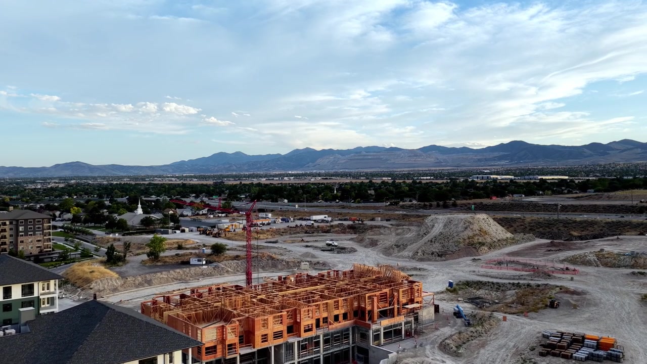 Wood-frame apartment construction project with tower crane, site roads, earthworks and residential neighborhoods in Taylorsville, Salt Lake County, Utah, beneath the Wasatch Range, drone push in.