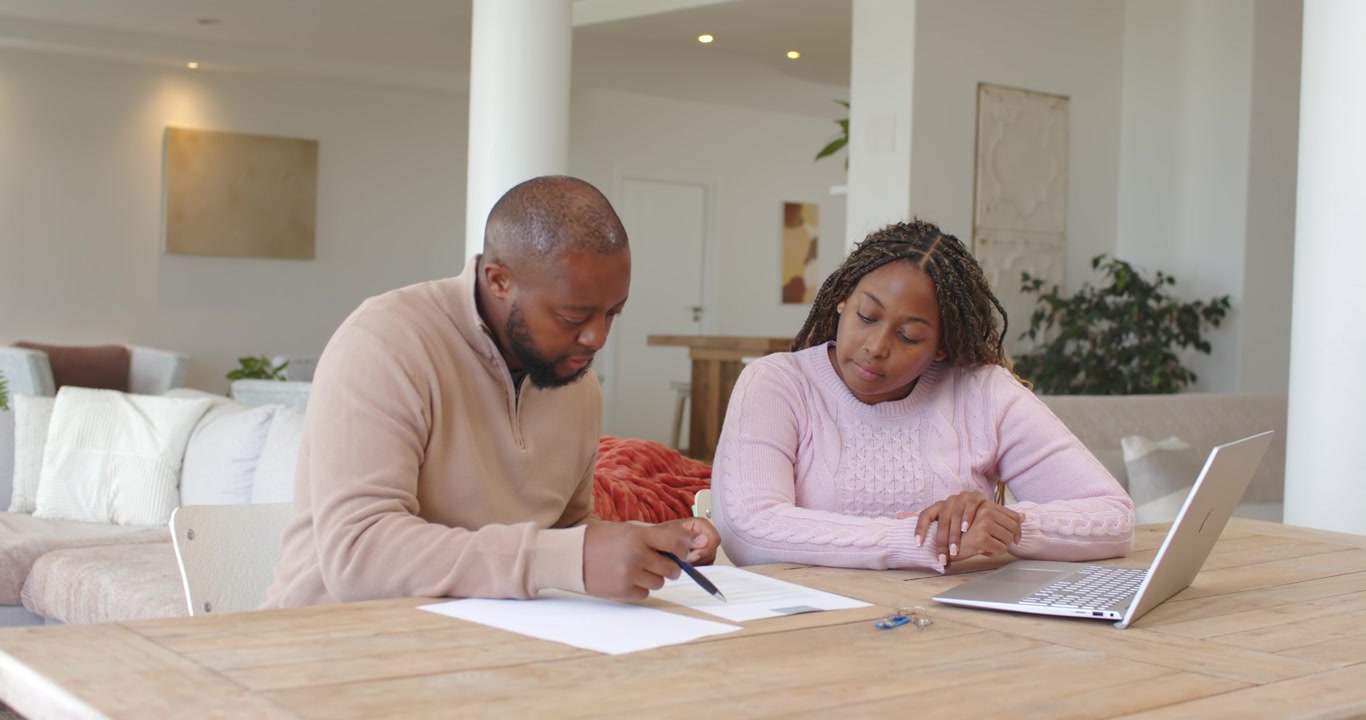 African American couple, man flipping papers at home, signing forms using pen to complete paperwork