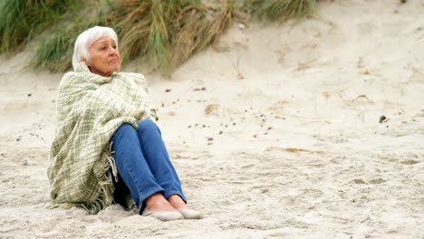 Thoughtful-retired-woman-sitting-on-the-beach