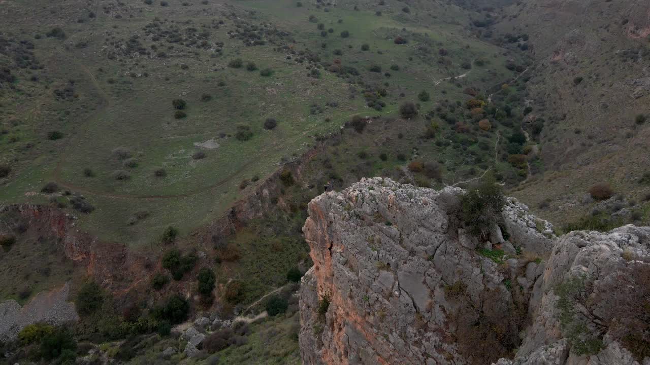 вид с воздуха на человека, сидящего на краю отвесной скалы и смотрящего вниз на долину