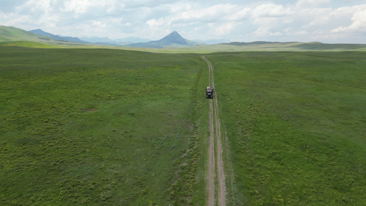산으로 둘러싸인 넓은 잔디 ⁇ 에서 자동차 트레일의 한가운데에 주차 된 버려진 준 트럭