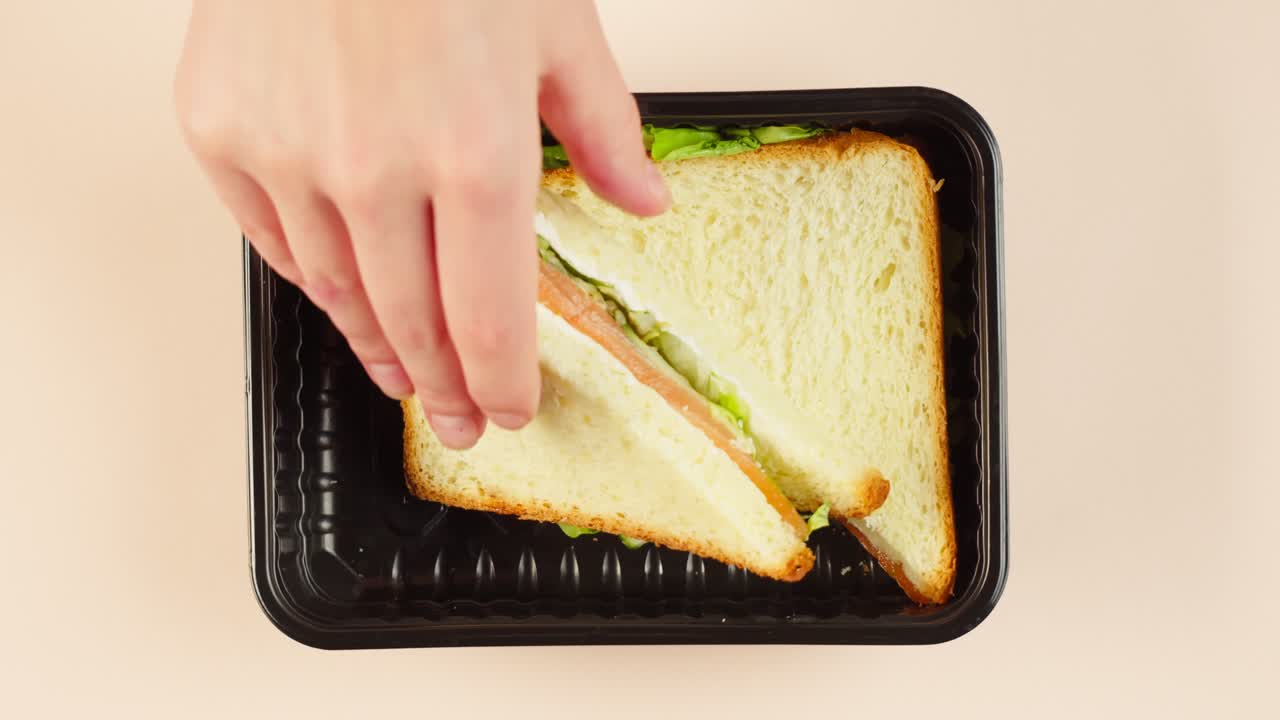 Mano che posiziona un panino fresco in un contenitore per asporto.