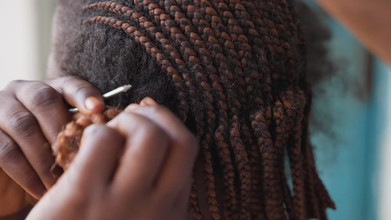 Primo piano di mani che intrecciano capelli testurizzati. Una stilista professionista lavora in una calda luce da studio, con le dita che separano le radici, aggiungendo extension all'uncinetto e ricci. Tensione e modellatura accurate, in un processo intimo e lento.
