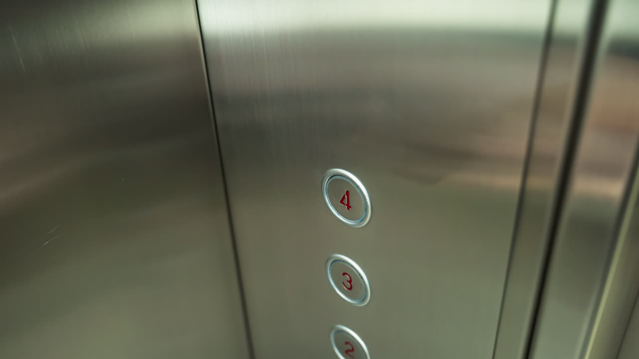 a finger pressing the number four button inside an elevator. The elevator panel is metallic with clearly marked floor numbers, showcasing modern elevator design and functionality