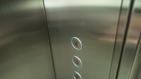 un dedo presionando el botón número cuatro dentro de un ascensor. el panel del ascensor es metálico con números de piso claramente marcados, mostrando el diseño y la funcionalidad moderna del ascensor