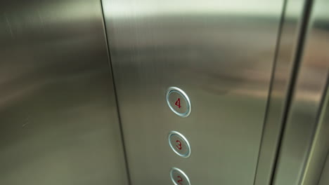 a finger pressing the number four button inside an elevator. the elevator panel is metallic with clearly marked floor numbers, showcasing modern elevator design and functionality