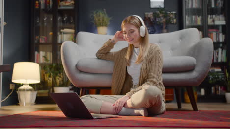 happy young woman with wireless headphones watching movie on laptop computer while sitting on floor at home