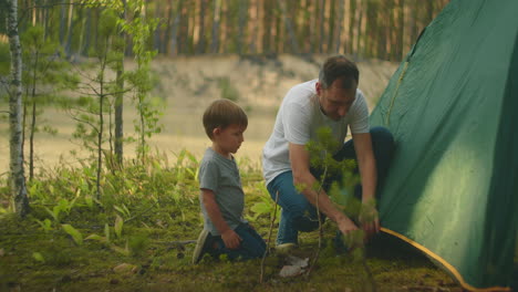 Tourists-in-the-forest-on-the-shore-of-the-lake-family-father-and-son-set-up-a-tent-camp-in-slow-motion