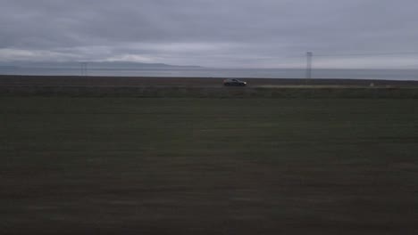 a drone follows a car driving through the tranquil evening, its headlights cutting a path through the merging colors of dusk
