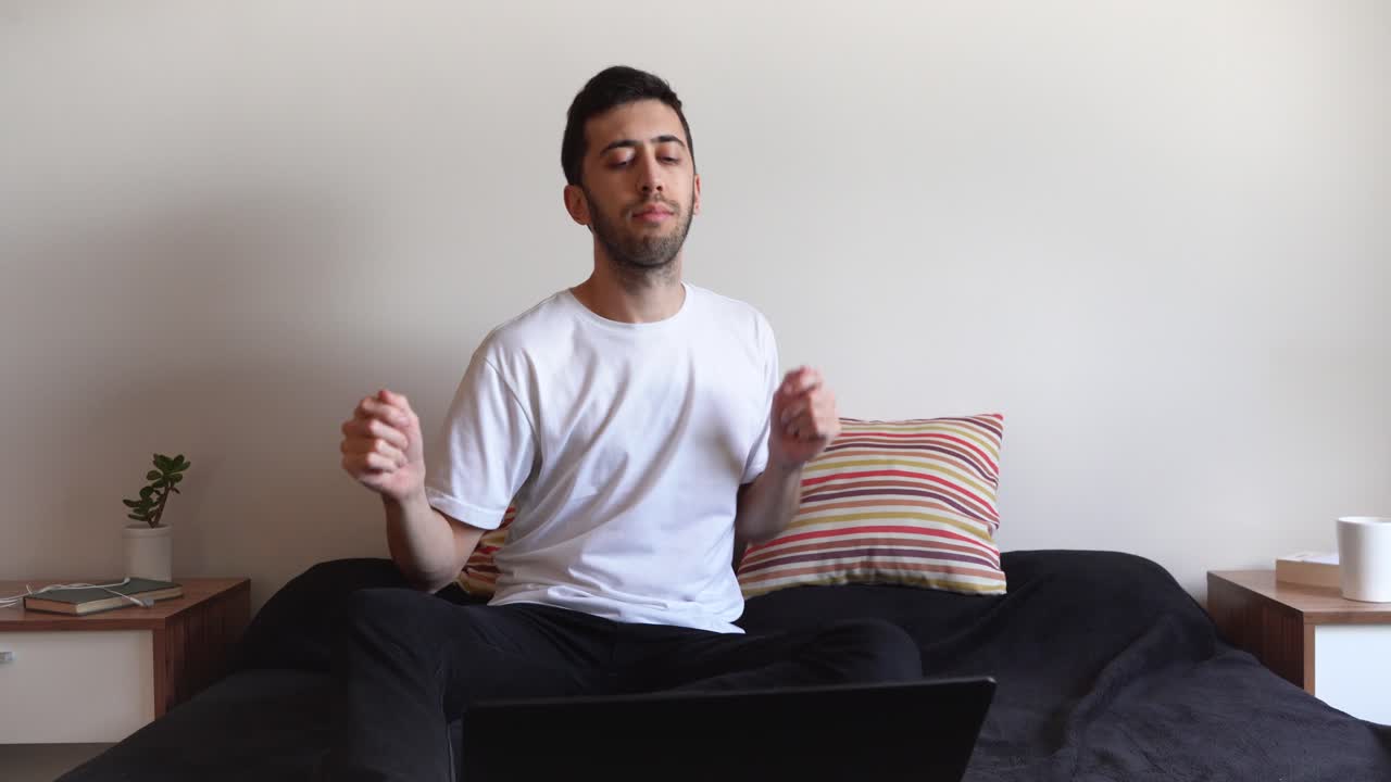 Happy man sitting on his bed and dancing in front of his laptop