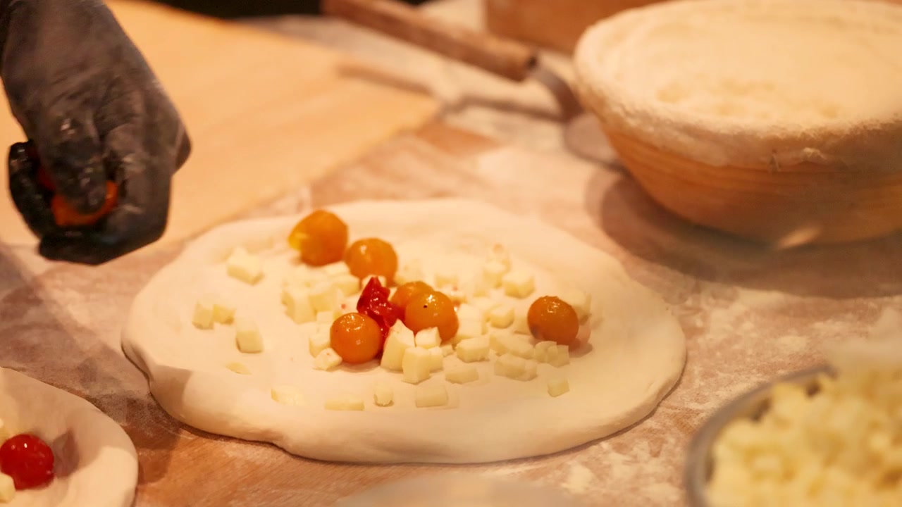Close-up shot of hands adding tomatoes to dough with cheese in a professional kitchen.