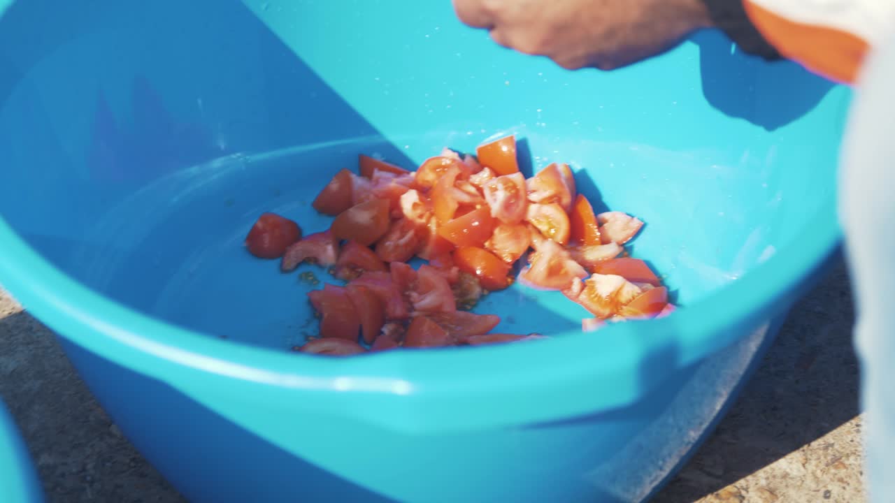 hombre cortando tomates en un recipiente de plástico usando un cuchillo sol al aire libre