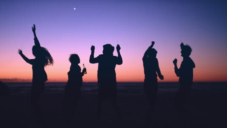 Eine-Gruppe-Von-Freunden-Tanzt-In-Der-Abenddämmerung-Am-Strand