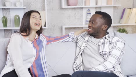 happy multiethnic couple in love sitting on sofa at home and having loving conversation.