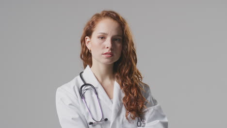 studio portrait of serious female doctor with stethoscope in white coat against plain background