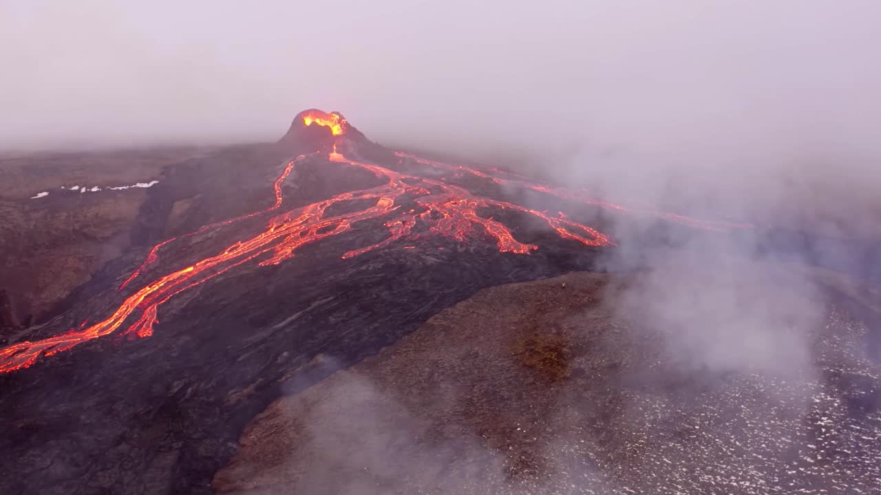 A high-resolution 4K drone captures cinematic aerial footage, presenting unique wide-angle shots of a landscape featuring a volcano and flowing lava, with swirling fog enveloping the scene