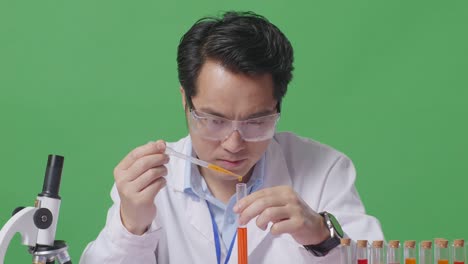 close up of asian man scientist sitting and making experiment with test tube on the table with microscope in the green screen background laboratory
