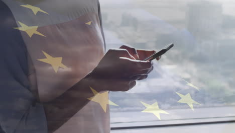 using smartphone, person standing by window over european union stars animation