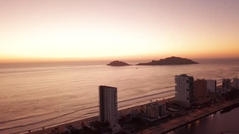 Volando-Hacia-Los-Hermosos-Edificios-De-Gran-Altura-Frente-A-La-Playa-Al-Atardecer