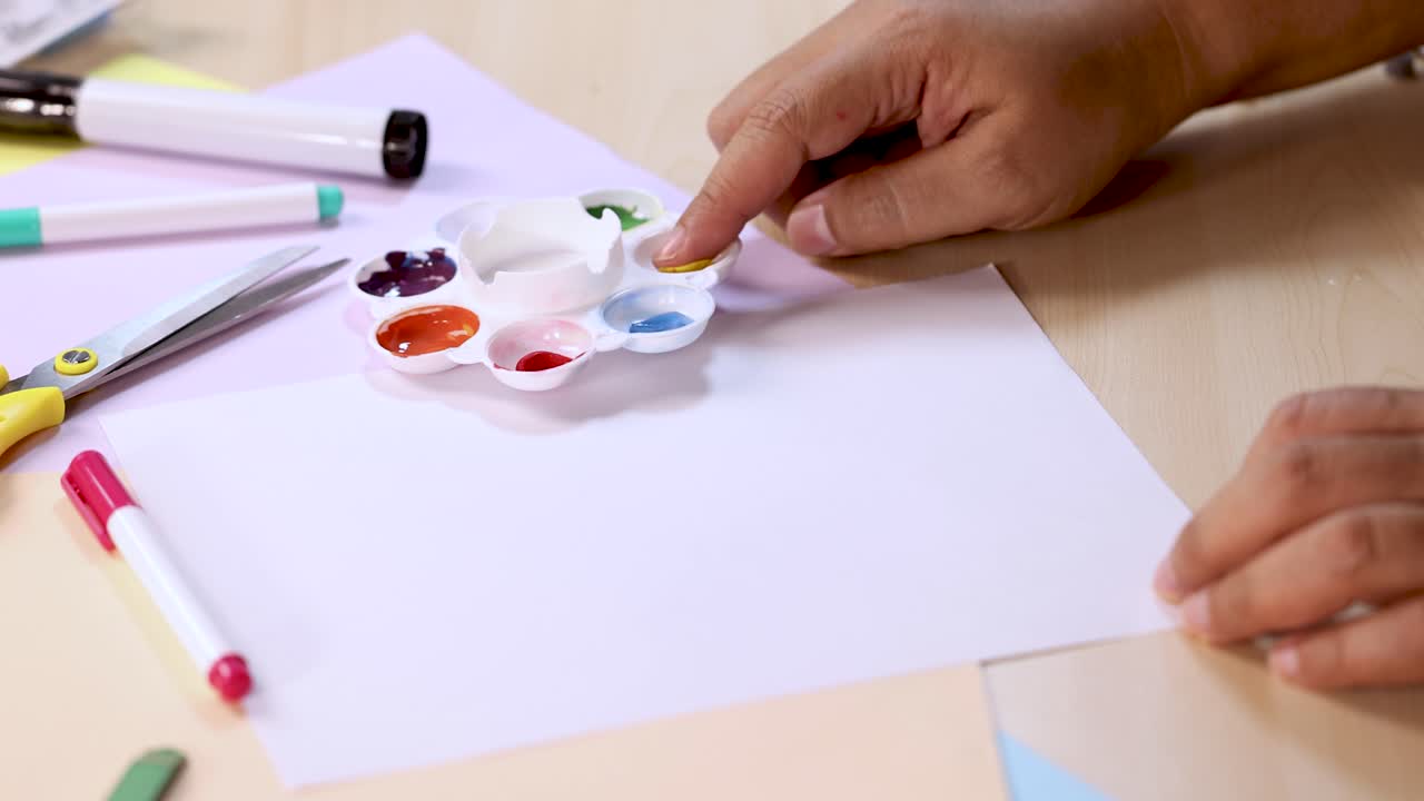 Hand dips finger in paint palette, dabs fingerprint onto white paper, bright indoor lighting